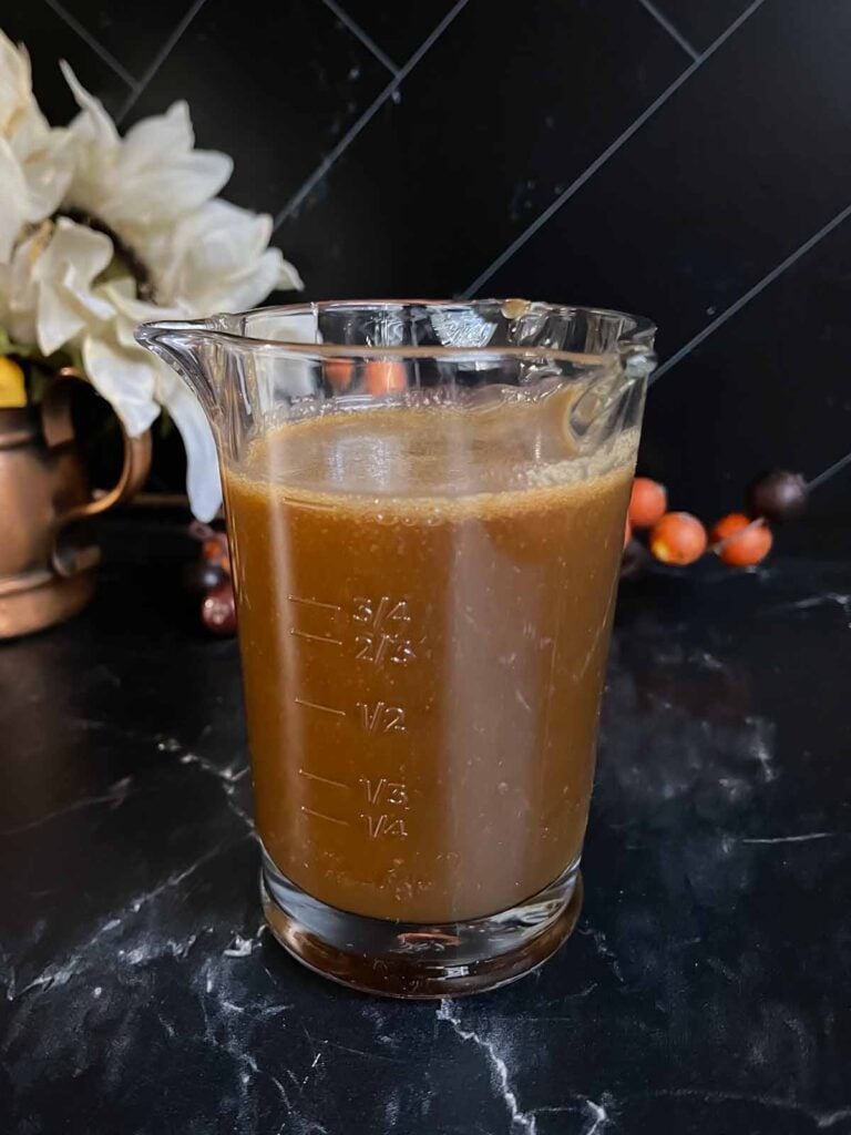 Salted caramel sauce in a glass measuring cup on a dark surface.