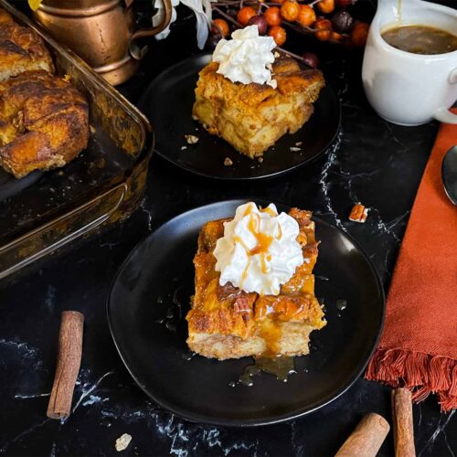 Slice of pumpkin bread pudding garnished with whipped cream and salted caramel sauce on a dark surface.