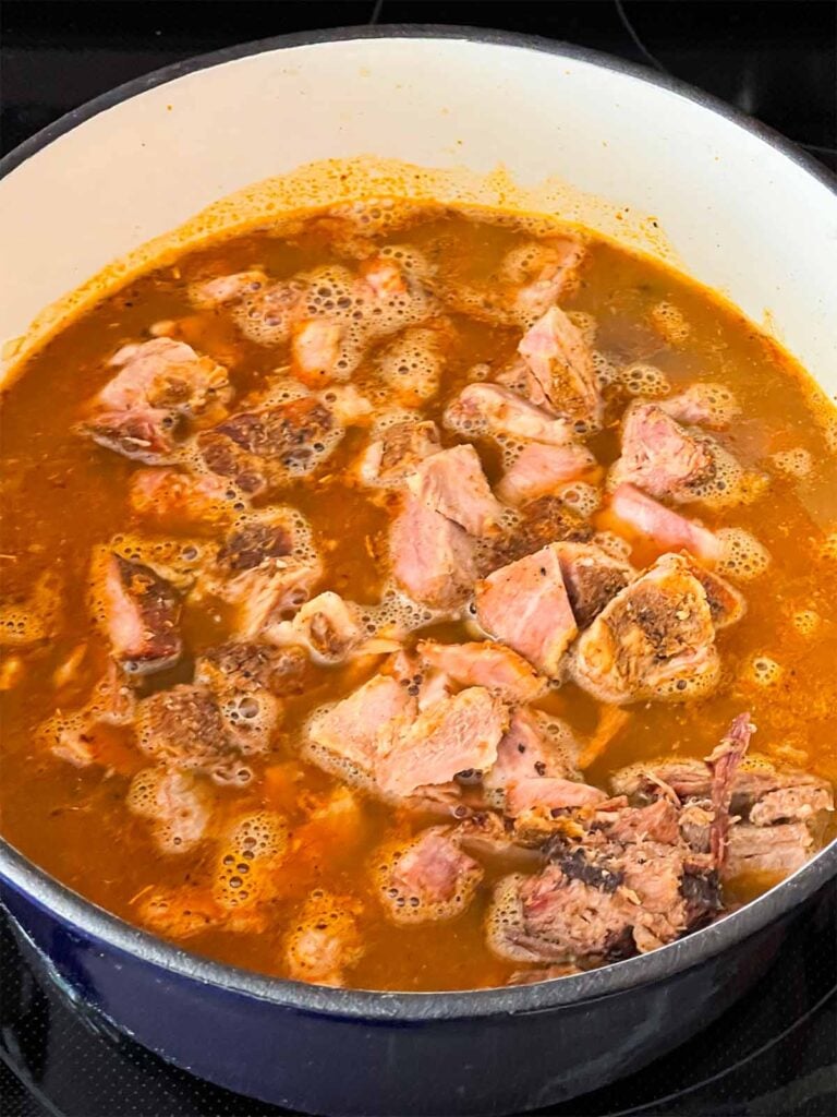 Smoked pork added to chili base in a dutch oven.