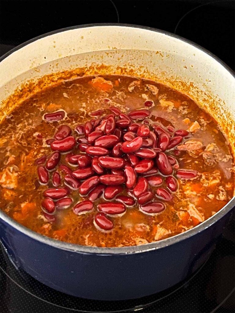 Adding pinto beans to smoked pork chili in a dutch oven.