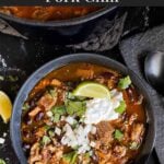 Smoked pork chili garnished with cilantro, onion, lime, sour cream, and onion in a dark bowl.