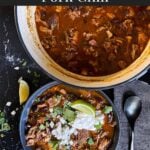 Smoked pork chili garnished with cilantro, onion, lime, sour cream, and onion in a dark bowl.