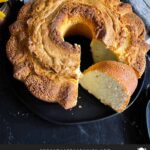 Pound cake on a black plate with one slice cut.