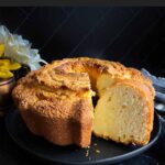 Pound cake on a black plate with one slice cut.