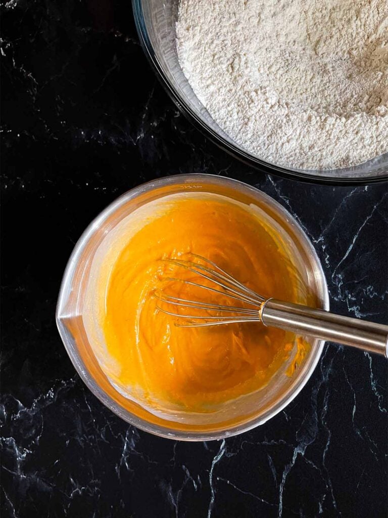 Buttermilk and sweet potato puree whisked together in a metal mixing bowl on a dark surface.