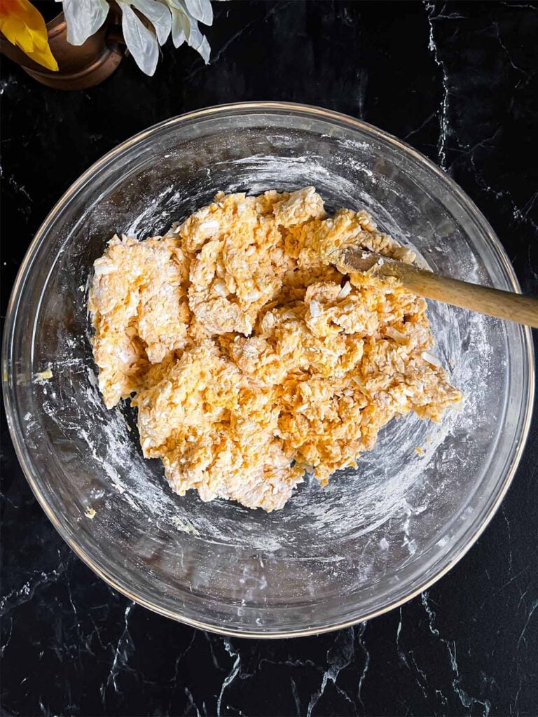 Sweet potato biscuit dough mixed in a glass mixing bowl on a dark surface.