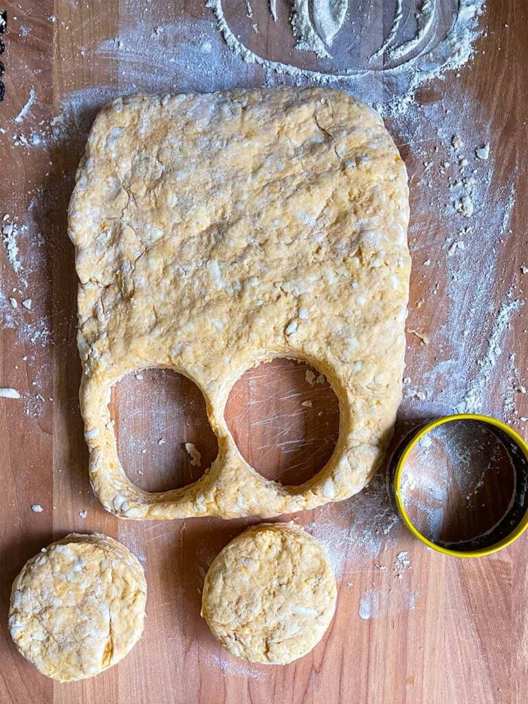 Sweet potato biscuit dough cut out into rounds on a floured wooden board.