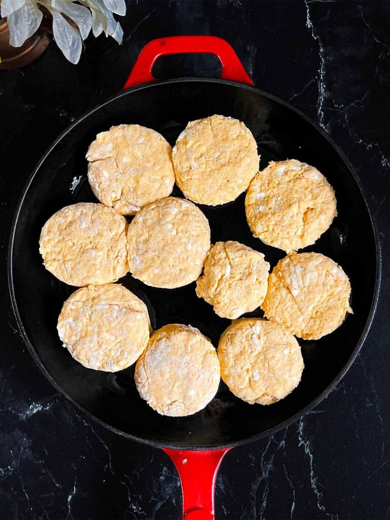 Unbaked sweet potato biscuits in a cast iron skillet on a dark surface.