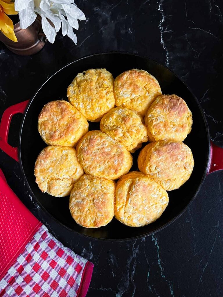 Baked sweet potato biscuits in a cast iron skillet on a dark surface.