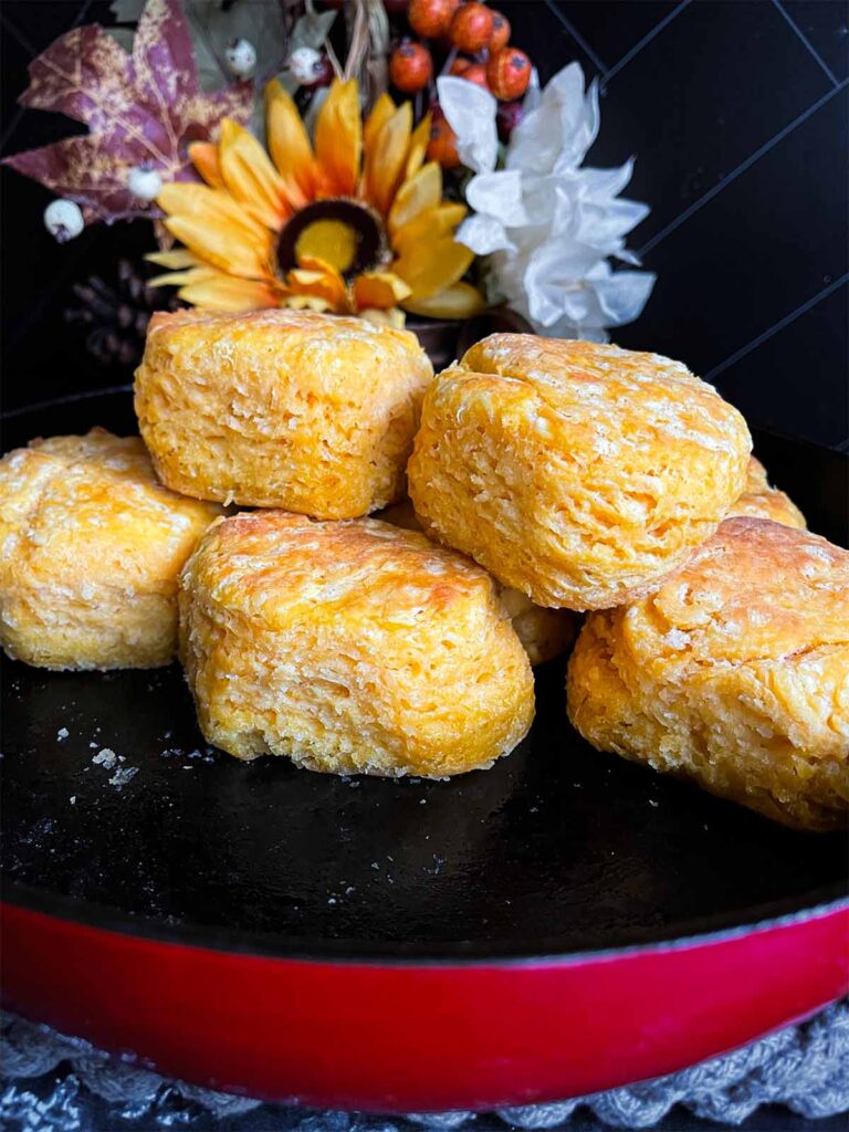 Baked sweet potato biscuits stacked in a cast iron skillet on a dark surface.