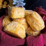 Baked sweet potato biscuits stacked in a bread basket, lined with a cloth napkin on a dark surface.