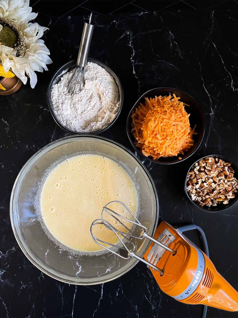 Wet ingredients for sweet potato cake combined in a large glass bowl on a dark surface.