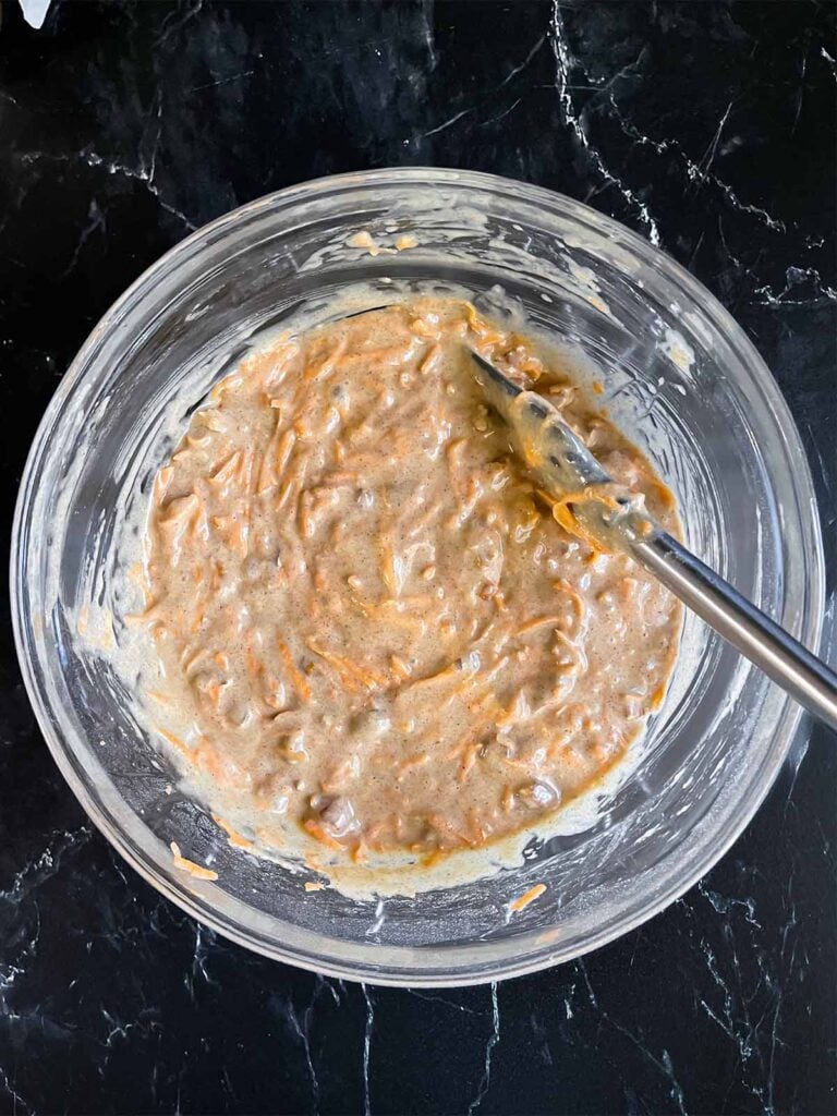 Sweet potato cake batter in a glass mixing bowl on a dark surface.