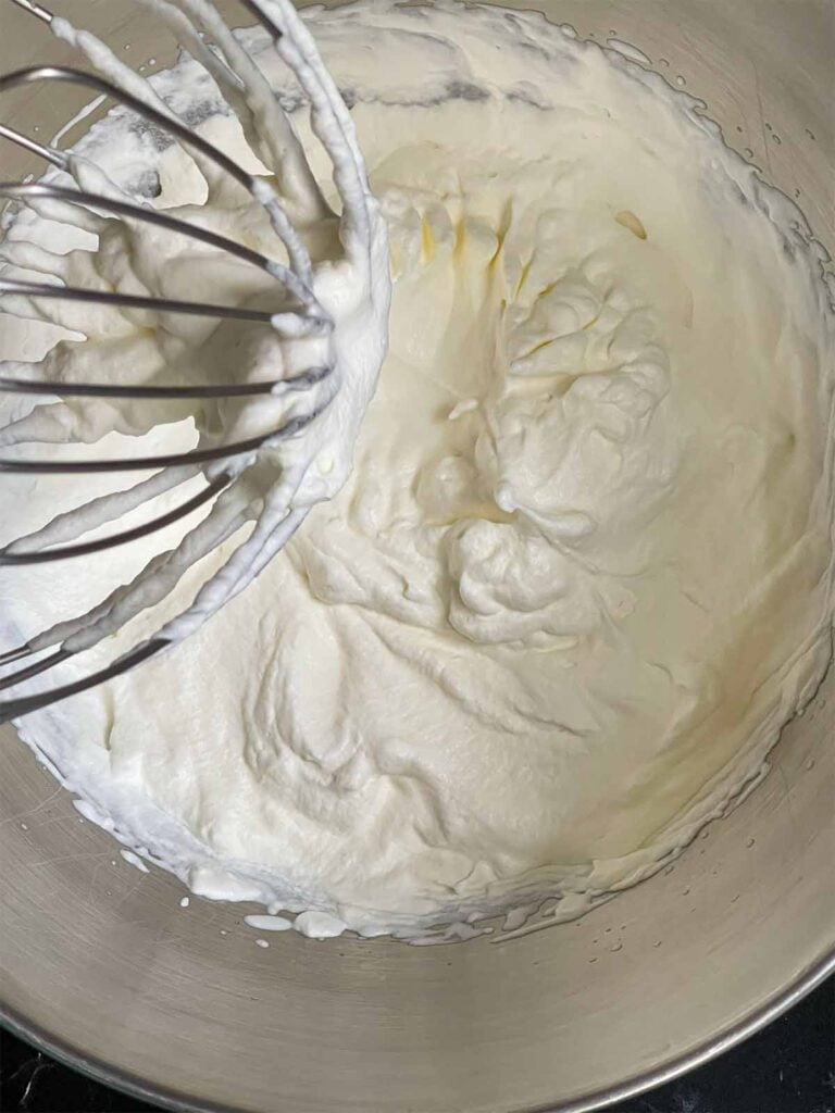 Heavy cream whipped to stiff peaks in a metal mixing bowl.