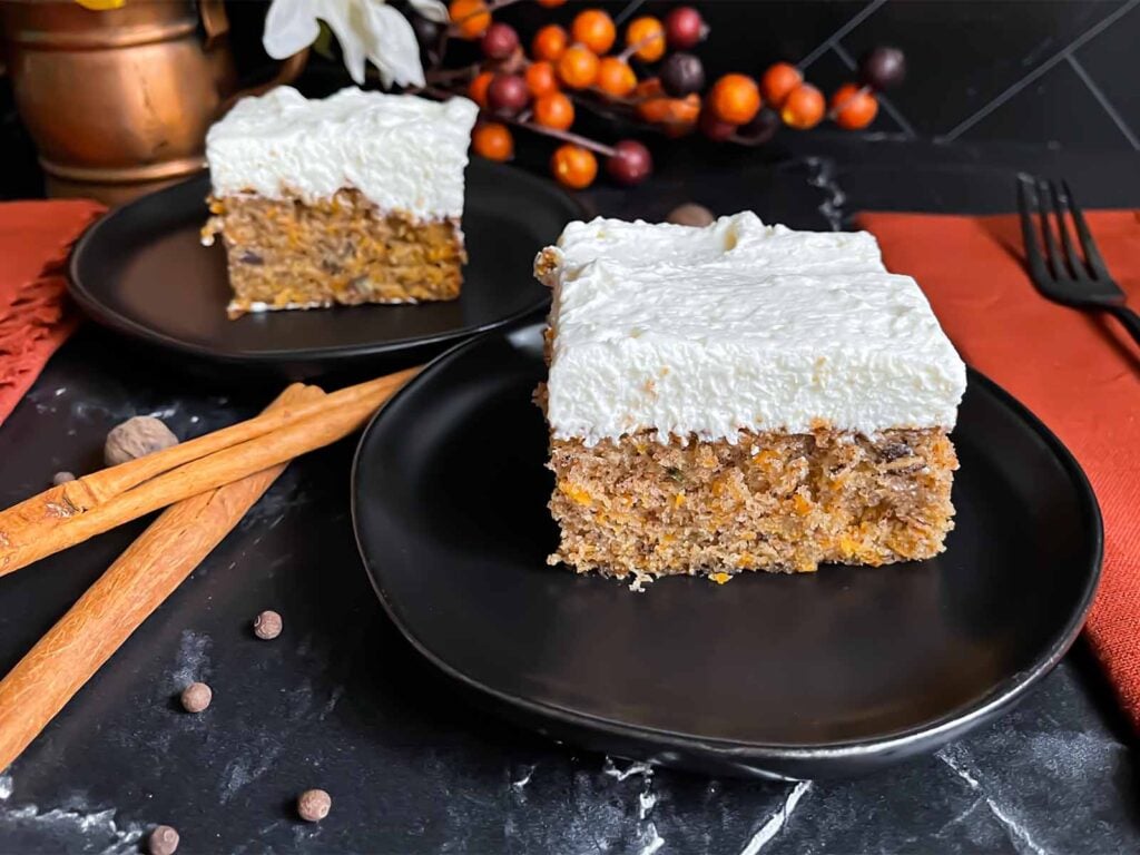 Two slices of sweet potato cake on dark plates on a dark surface.