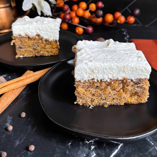 Two slices of sweet potato cake on dark plates on a dark surface.