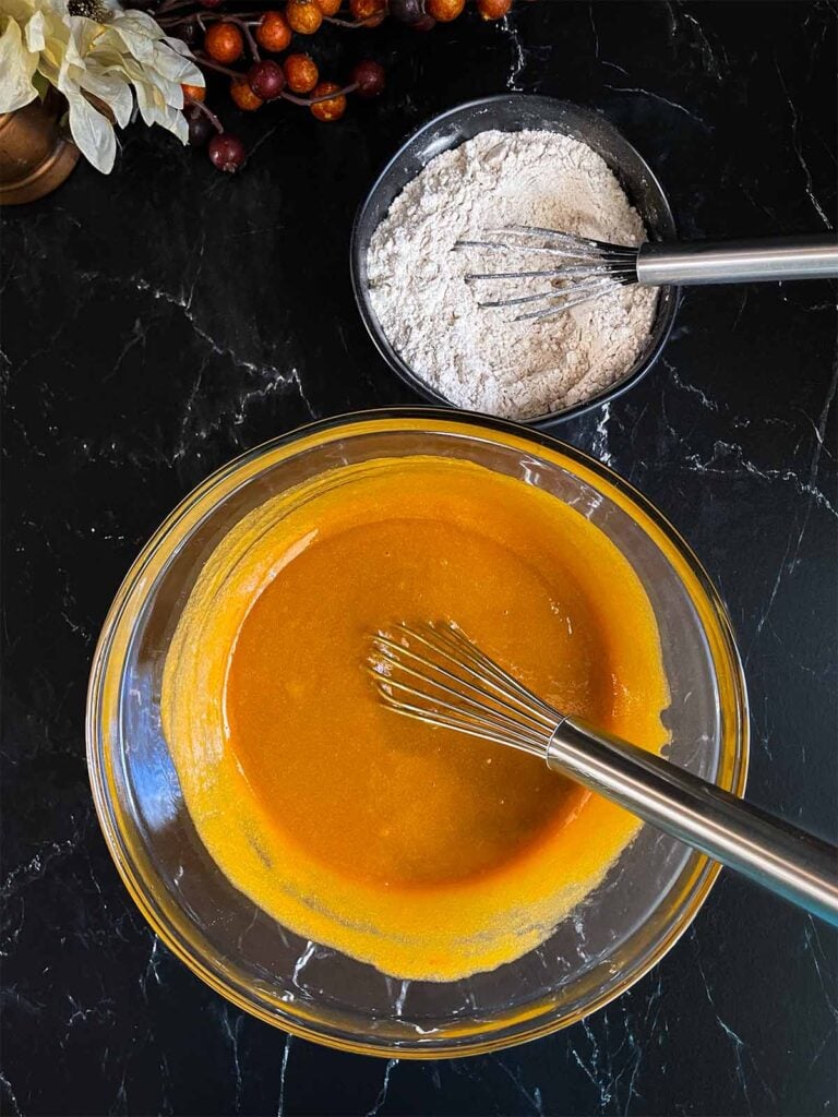 Combined wet ingredients for sweet potato muffins in a large glass bowl on a dark surface.