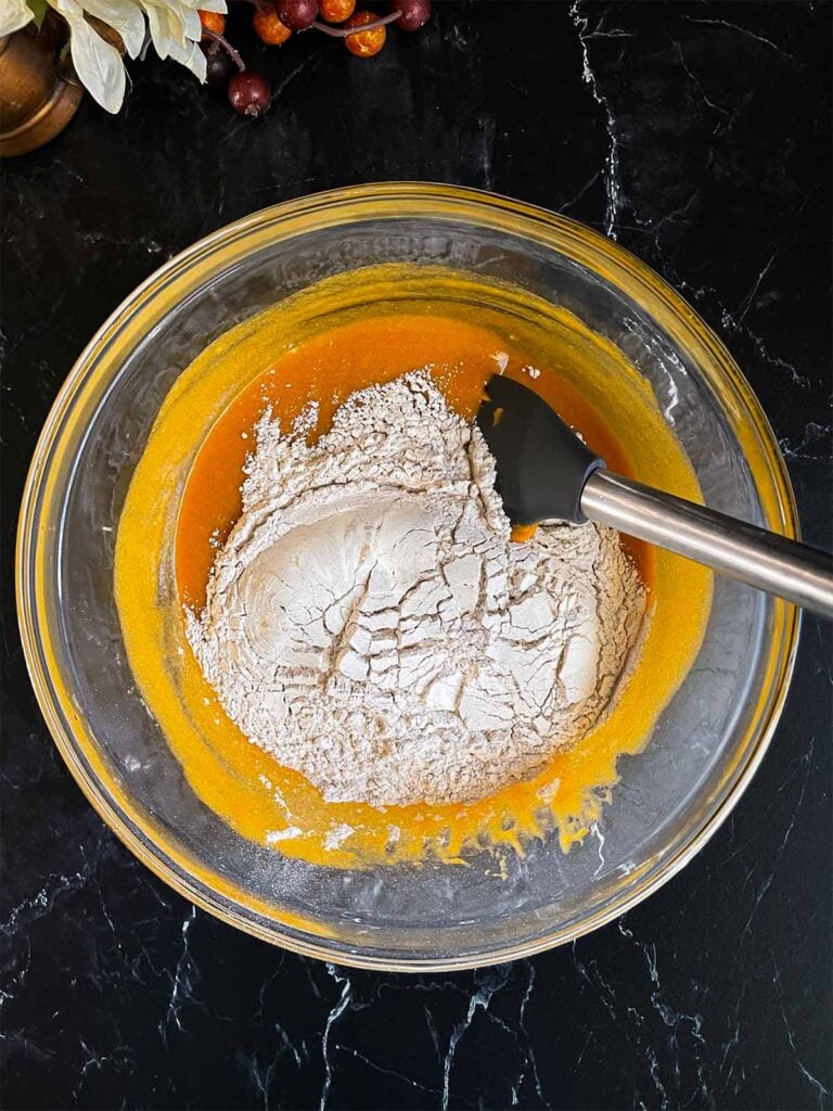 The dry ingredients added to the wet ingredients in a large glass bowl for sweet potato muffins.