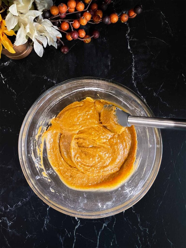 Sweet potato muffins batter mixed in a large glass bowl on a dark surface.
