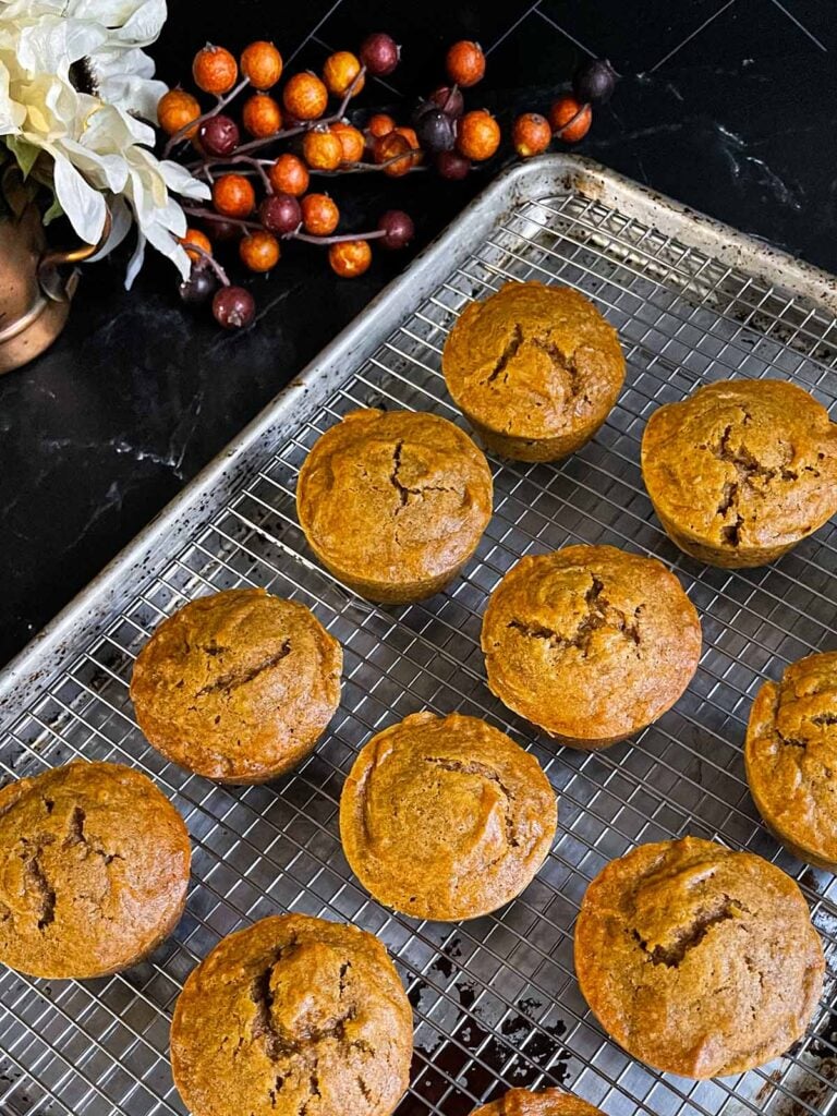 Sweet potato muffins on a wire rack inside a baking sheet on a dark surface.