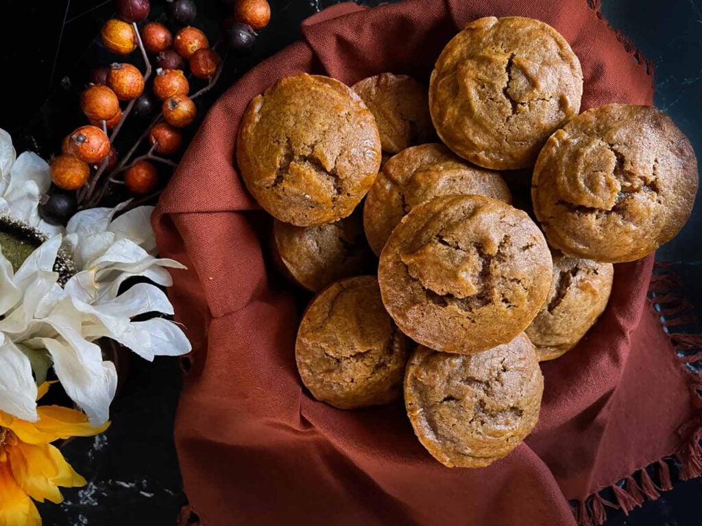 Sweet potato muffins in an orange cloth lined basket with flowers on the side.