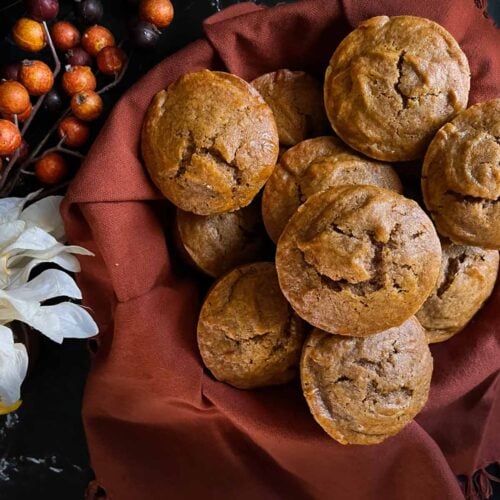 Sweet potato muffins in an orange cloth lined basket with flowers on the side.