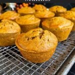 Sweet potato muffins on a wire rack inside a baking sheet on a dark surface.