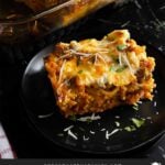 A serving of baked spaghetti on a dark plate with the casserole in the background.