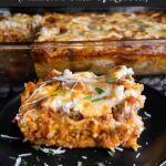 A serving of baked spaghetti on a dark plate with the casserole in the background.