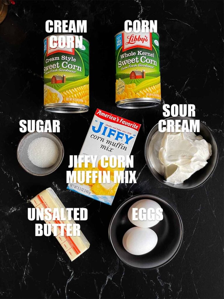 Ingredients needed to make corn casserole on a dark surface.