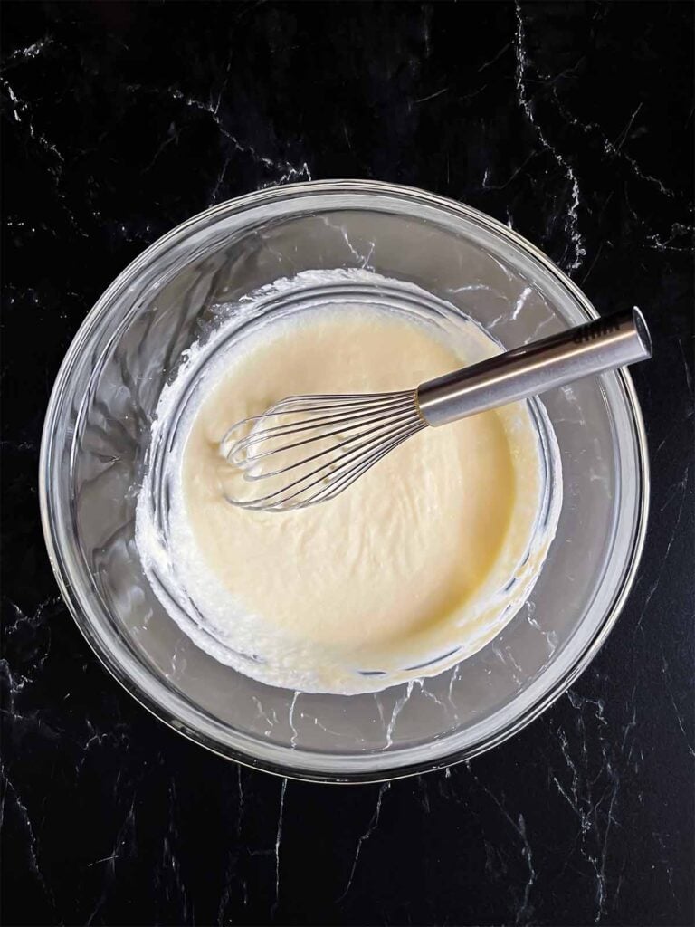 Corn casserole wet ingredients whisked together in a glass mixing bowl.