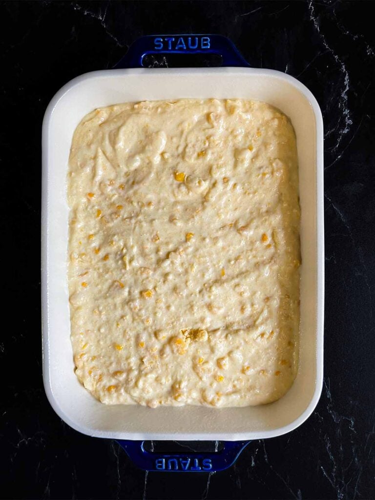 Corn casserole batter in a baking pan on a dark surface.