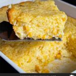 A serving of creamy corn casserole lifted over the baking pan on a dark surface.
