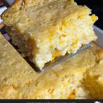 A serving of creamy corn casserole lifted over the baking pan on a dark surface.