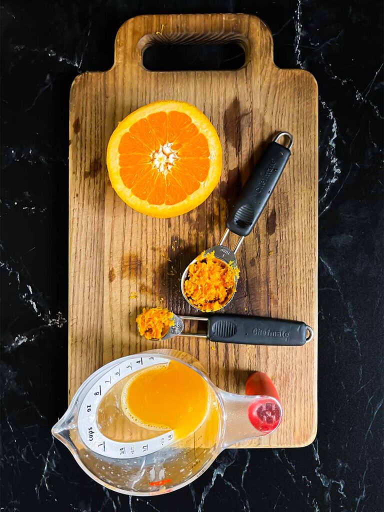 Orange zest and fresh orange juice on a wooden cutting board.