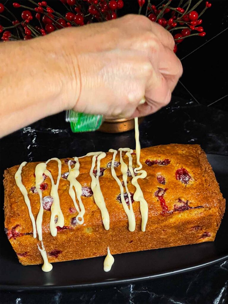 Icing being drizzled onto a freshly baked loaf of Cranberry Orange bread.