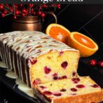 Cranberry Orange bread with an orange glaze on a dark surface with one slice laying on its side showing the interior.