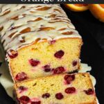 Cranberry Orange bread with an orange glaze on a dark surface with one slice laying on its side showing the interior.