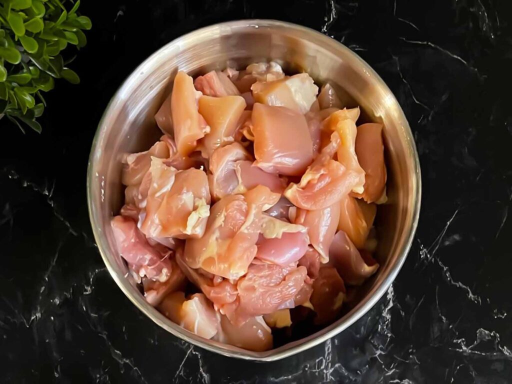 Cubed chicken thighs in a stainless steel bowl on a dark surface.