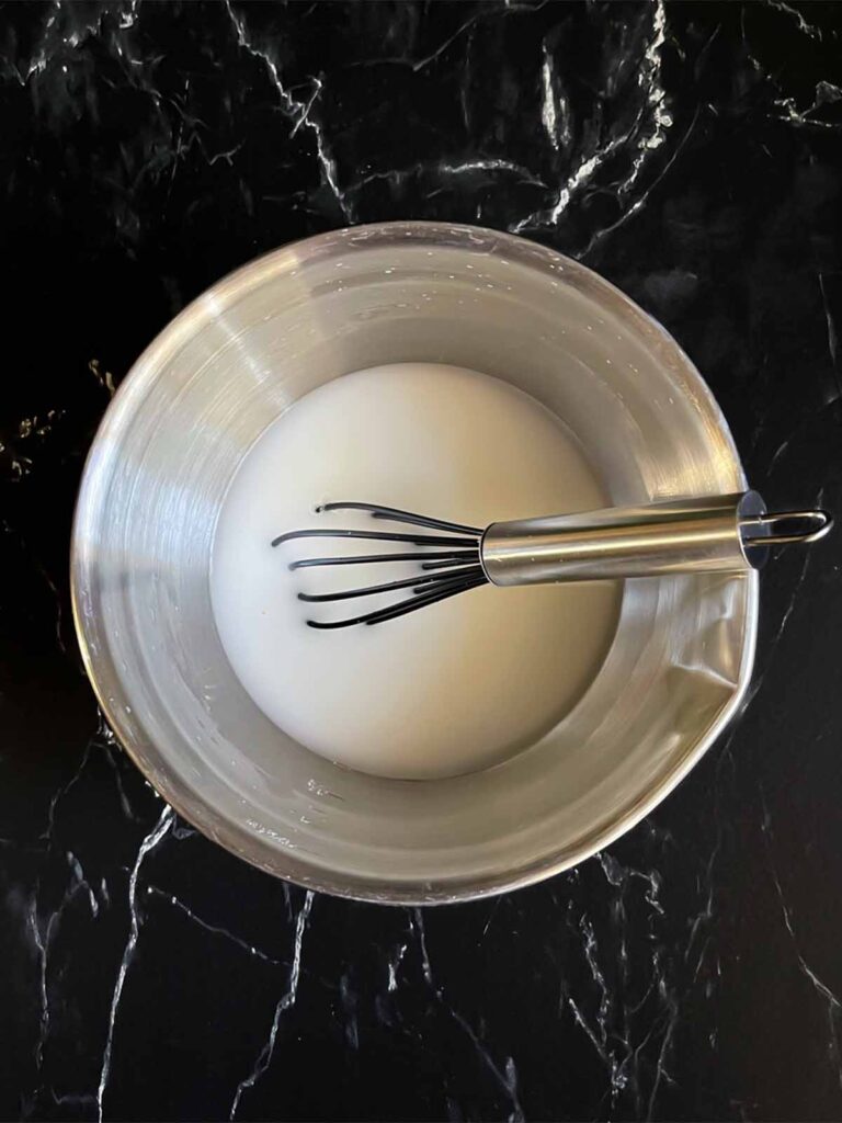 Water and cornstarch slurry in an aluminum bowl on a dark surface.