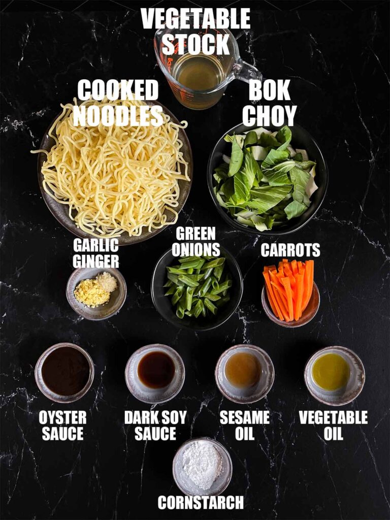 Ingredients needed to make vegetable lo mein on a dark surface.