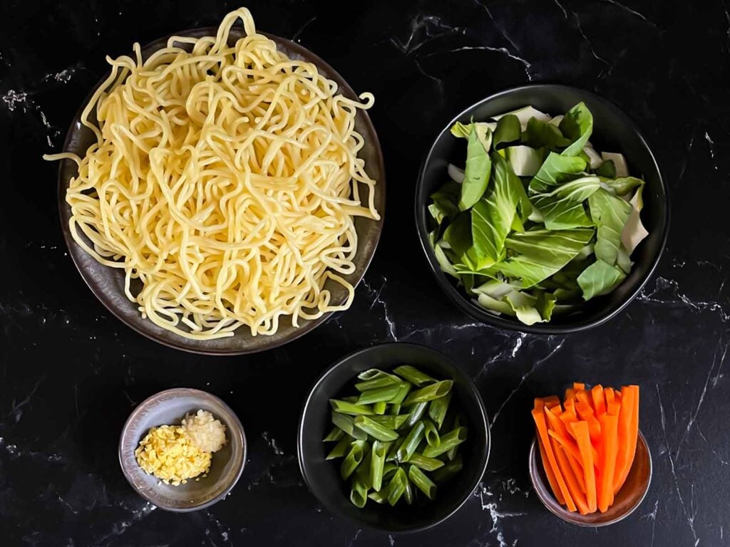Ingredients for a lo mein dish on a dark surface.