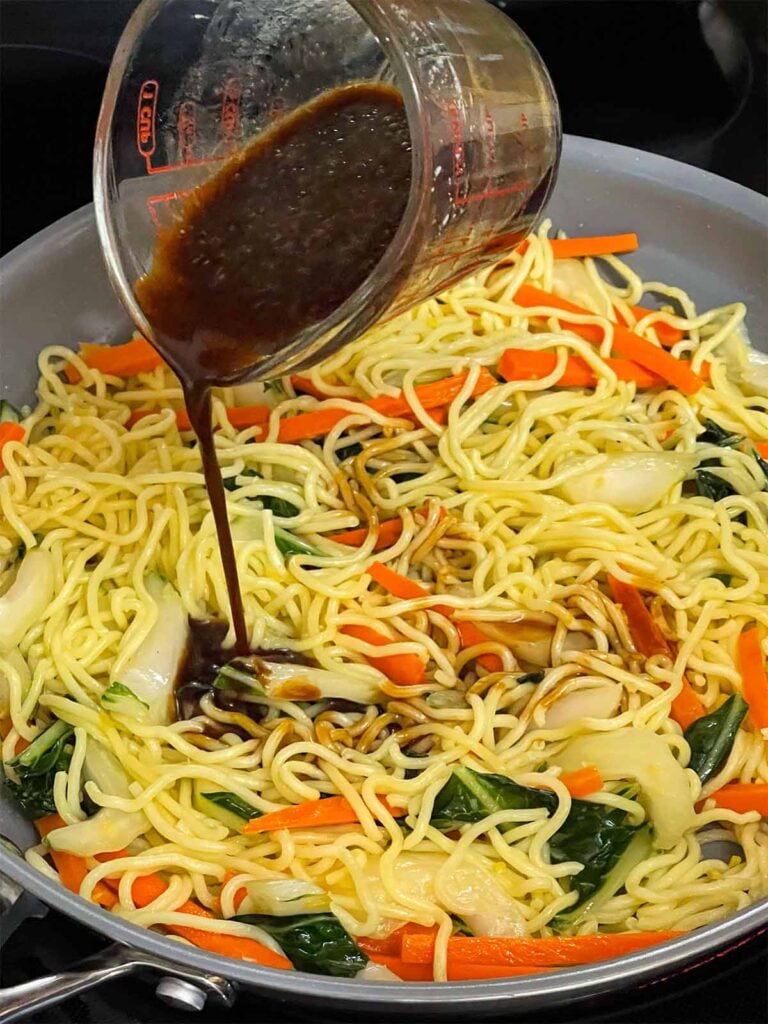 Adding a sauce to lo mein in a skillet.