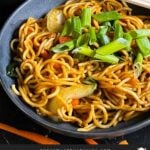 Vegetable lo mein garnished with green onion in a dark bowl.