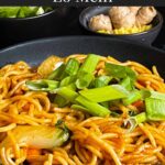 Vegetable lo mein garnished with green onion in a dark bowl.