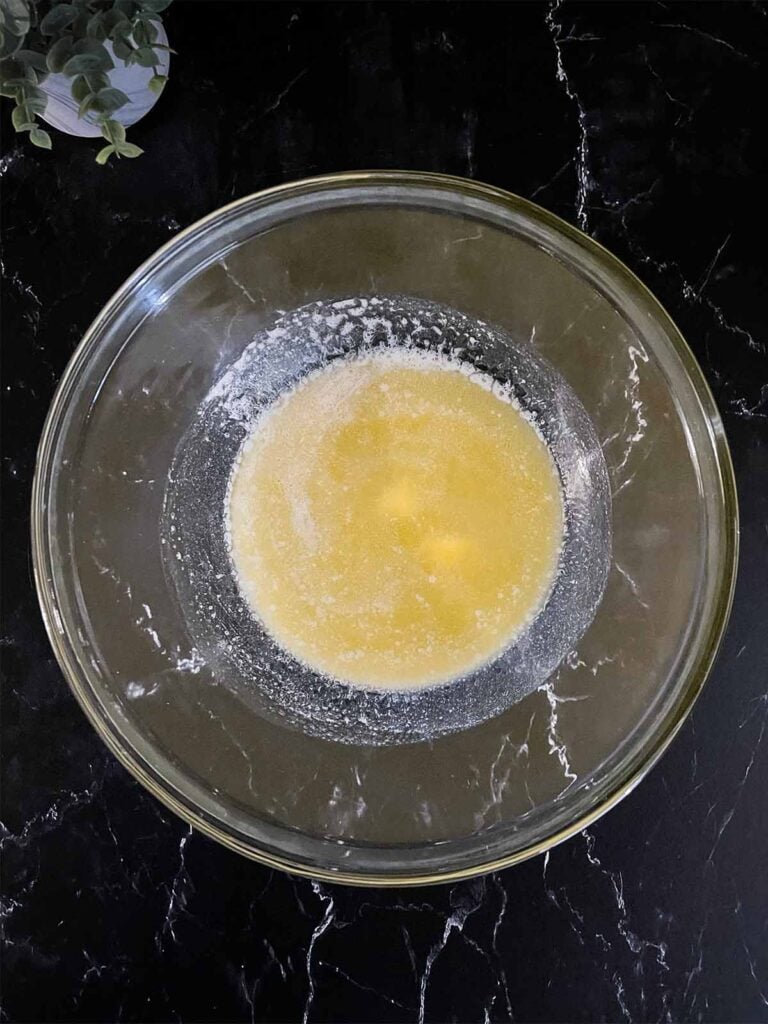 Melted butter in a glass mixing bowl on a dark surface.
