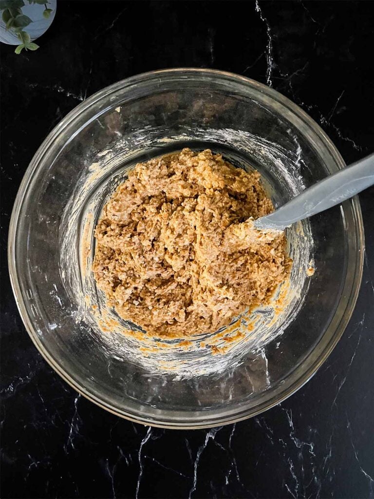 Peanut butter pretzel bar mixture in a glass mixing bowl on a dark surface.