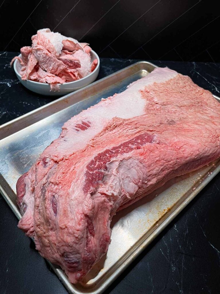 A trimmed brisket on a sheet pan with scraps in the background.