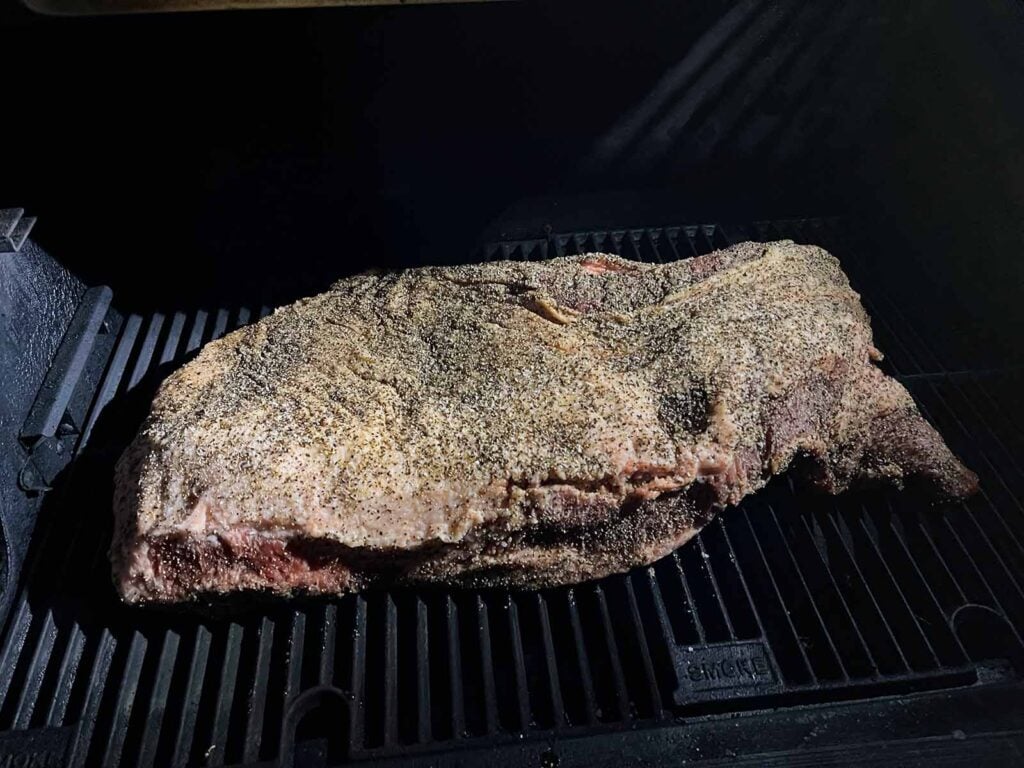 A brisket, fat side up, just placed on a smoker.
