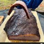 A slice of brisket flat being balanced on a gloved finger.